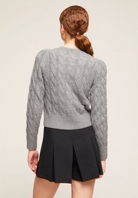 Šedý svetr s pleteným vzorem a dlouhými rukávy, s ribbovaným lemem, ve spojení s černou skládací sukní. Textura je měkká a útulná.