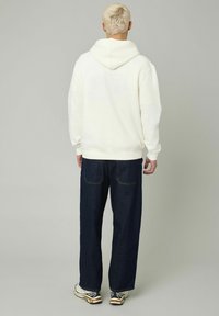 Sweat à capuche blanc avec une poche kangourou, coupe spacieuse. Associé à un jean large bleu foncé et des baskets avec des accents noirs et blancs.