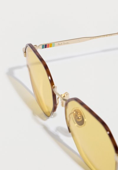 Occhiali da sole tartarugati marroni con montatura in metallo dorato. Lenti con tintura gialla, con un accento a strisce colorate sulla stanghetta con marchio.