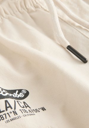 Beiga shorts i bomull med dragsko i midjan och svarta snörändar; har tryckt text på framsidan.