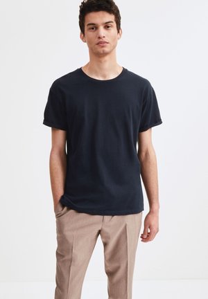 T-shirt nera a maniche corte in cotone, scollatura rotonda, vestibilità rilassata, abbinata a pantaloni chiari e sartoriali. Design semplice e classico.