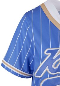 Maglia blu chiaro con strisce verticali bianche, presenta colletto e bordi delle maniche beige, con ricamo dorato sulla parte anteriore.