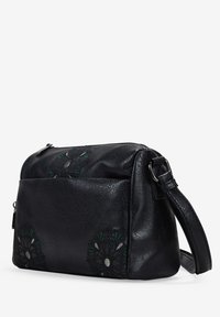 Bolso bandolera de piel negra con acentos de bordado floral, forma rectangular, cierre de cremallera y correa ajustable. Detalle de superficie texturizada.
