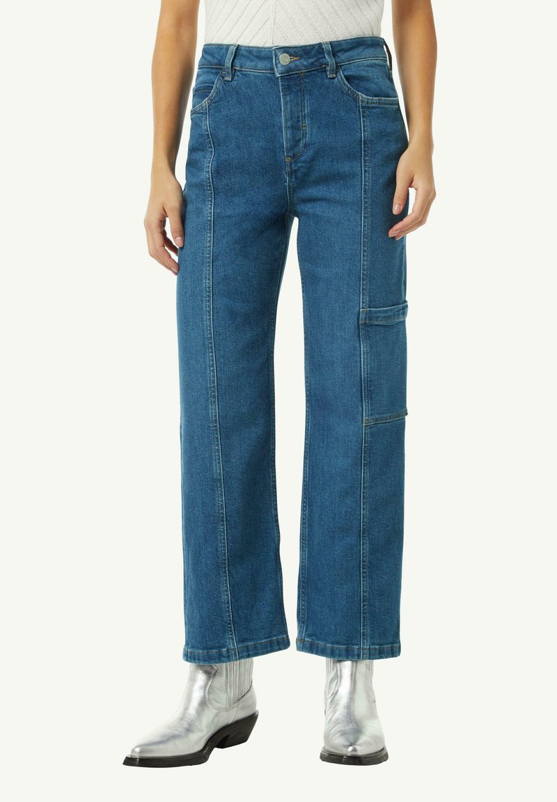 Jasnoniebieskie dżinsy z wysokim stanem, szeroką nogawką i boczną kieszenią cargo. Posiadają widoczne szycia, klasyczne zapięcie na guzik oraz szlufki na pasek.