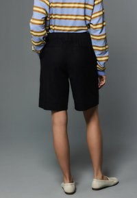 Pantaloni scurți negri, cu croială lejeră, având talie elastică și două buzunare la spate, asortați cu un top cu mâneci lungi, cu dungi multicolore.