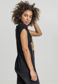 Svart bomull T-skjorte med rullede ermer, som har et grafisk design på forsiden. Stoffet ser mykt og lett ut.