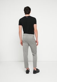 Maglietta aderente nera e pantaloni grigi a vita alta con sottili righe. Calzature nere. Vista posteriore su sfondo neutro.