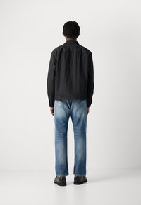 Svart lett jakke med krage, kombinert med blå denimjeans med falmet finish og rett ben. Sorte sko fullfører antrekket.
