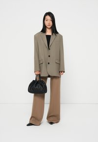 Oversized beige blazer met twee zwarte knopen, zwart topje eronder, bruine brede broek en een kleine zwarte gehaakte handtas.