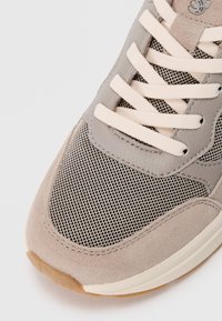 Graue Sneaker aus einer Kombination von Wildleder und Mesh-Materialien, mit einer strukturierten Oberfläche, gepolsterter Zunge und beigen Schnürsenkeln.