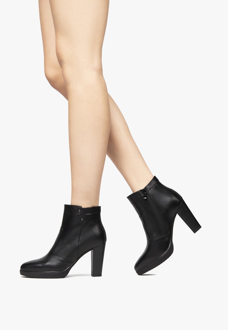 Bottes de cheville en cuir noir avec un talon block haut, fermeture éclair latérale et texture lisse. Présente un bout arrondi et des détails de couture minimalistes.