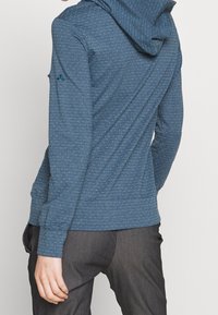 Hoodie v modré barvě s jemnými bílými puntíky, měkká látka, padnoucí střih a žebrované manžety. Kombinováno se šedými kalhotami.