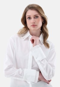 Camicia bianca con bottoni, colletto e polsini impreziositi, caratterizzata da una texture liscia e un design classico. Stile minimalista, senza pattern.