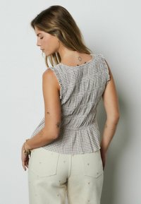 Ruuduline pruuni ja kreemika peplum-tüüp rüüsidega kaelusega; sobitatud kreemja südame mustriga pükstega. Sile tekstuur.