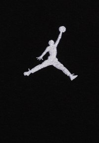 Silhouette di un giocatore di basket che salta con le gambe divaricate, raggiungendo in alto per tenere un pallone da basket in una mano su un tessuto nero.