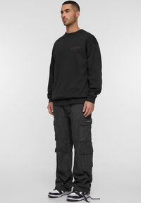 Hanorac negru cu guler rotund și logo purpuriu, asortat cu pantaloni cargo de culoare gri închis; pantalonii au multiple buzunare și un croi confortabil.