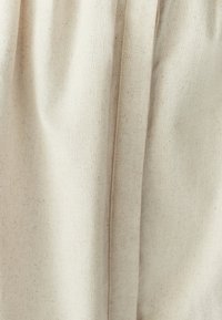 Tissu beige clair avec une finition texturée, présentant des drapés doux et fluides ainsi que des plis subtils. Design uni sans motifs ni accents.