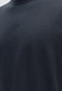 Κοντινό πλάνο σκουρόγριου T-shirt με διακριτικό λογότυπο και ανάγλυφο κείμενο "Est. 2016" στο στήθος.