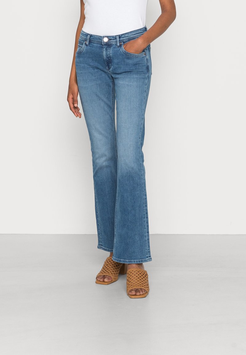 Jeans bleus évasés avec un léger dégradé, en coton, cinq poches et une fermeture à bouton à l'avant, associés à des sandales tressées marron.