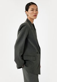 Grå blazer med en skræddersyet pasform, strukturerede skuldre, to knapper og sidelommer, lavet af tekstureret stof, parret med matchende bukser.