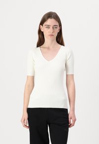 Gerippte, kurzärmlige Bluse in Creme mit V-Ausschnitt, die eine figurbetonte Silhouette und strukturierten Stoff aufweist.