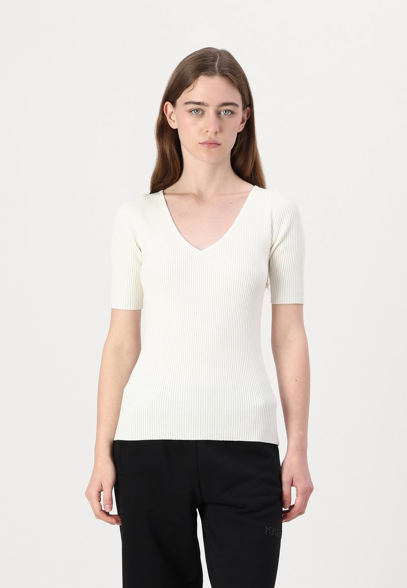 Gerippte, kurzärmlige Bluse in Creme mit V-Ausschnitt, die eine figurbetonte Silhouette und strukturierten Stoff aufweist.