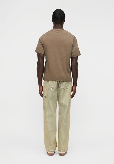 Καφέ κοντομάνικο T-shirt συνδυασμένο με ανοιχτό πράσινο τζιν παντελόνι με φαρδιά πόδια, που διαθέτει υφασμάτινη υφή, πίσω τσέπες και πλευρικό φερμουάρ.