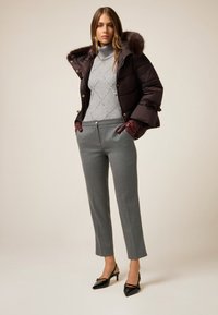 Brązowa kurtka puchowa z kapturem wykończonym futrem, szary sweter dzianinowy z wzorem w diamenty, szare spodnie o kroju dopasowanym oraz czarne szpilki z ostrym noskiem.