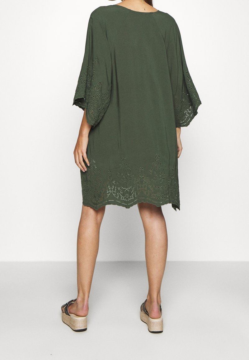 Olivgrünes Tunika-Kleid mit lockeren, ellbogenlangen Ärmeln und einem detaillierten Spitzenabschluss. Weicher Stoff mit entspannter Passform und rundem Halsausschnitt.