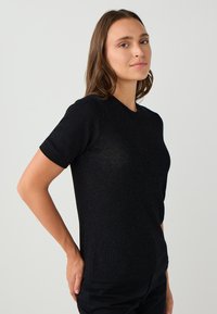 T-shirt nero a maniche corte in maglia con collo tondo, presenta una lucentezza sottile, un design aderente e una texture liscia. Nessun motivo o accessorio prominente.