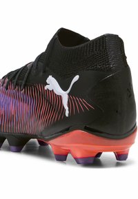 Crampons de football noirs avec un dessus texturé, des rayures dégradées violettes et rouges, un logo blanc et une semelle orange-rouge avec des crampons coniques pour une meilleure traction.