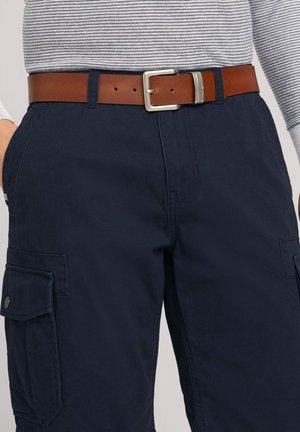 Pantalons cargo bleu marine avec poches latérales, associés à une ceinture en cuir marron avec une boucle en métal. Haut rayé visible au niveau de la taille.