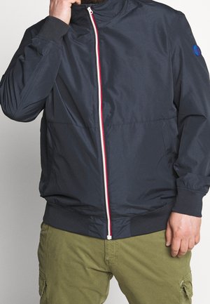 Veste bomber bleu marine en tissu lisse avec un col montant, dotée d'une fermeture éclair rouge et blanche et de poignets et ourlet côtelés.
