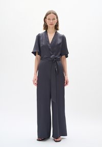 Tuta grigio scuro realizzata in tessuto morbido, con design avvolgente, maniche ampie, vita legata e pantaloni a gamba larga.