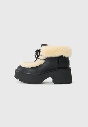Zwarte platformenkelschoenen met een gestructureerde leren afwerking, voorzien van een zachte crèmekleurige schapenvacht manchet en zwarte veters.