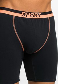 Shorts sportivi neri con una fascia arancione "SPORT", cuciture a contrasto e una vestibilità aderente progettata per il comfort.