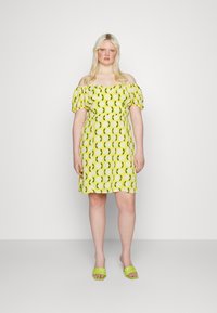 Vestido de ombros à mostra em amarelo com padrão floral branco e detalhes verdes; comprimento curto e mangas bufantes, combinado com sandálias verdes de slide.