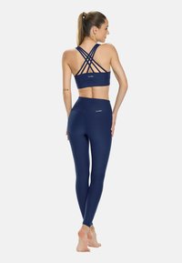 Námořnická sportovní podprsenka s křížovými ramínky a logem. V kombinaci s vysoko pasovými námořnickými legínami, obě vyrobeny z hladkého, elastického materiálu.