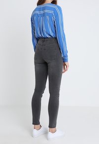 Jeans ajustados grises combinados con una camisa de botones a rayas azules, con mangas largas y un cuello estándar. El modelo lleva zapatillas blancas.