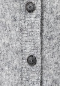 Cardigan gris de punto con una textura suave, dos botones negros prominentes y un borde acanalado, que destaca un diseño acogedor.