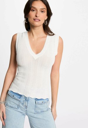 Top bianco senza maniche, con scollatura a V e un motivo a zigzag testurizzato, abbinato a jeans azzurri chiari a vita alta con tasche a toppa.