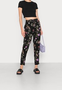 Svarta blommiga byxor med flerfärgade blommönster, med dragsko i midjan. Kombineras med en svart crop top och svarta sandaler.