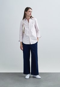 Ριγέ μακρυμάνικο πουκάμισο σε ανοιχτό ροζ και λευκό, συνδυασμένο με φαρδιά μπλε σκούρα παντελόνια και λευκά αθλητικά παπούτσια. Απλά κοσμήματα αναδεικνύουν το ντύσιμο.