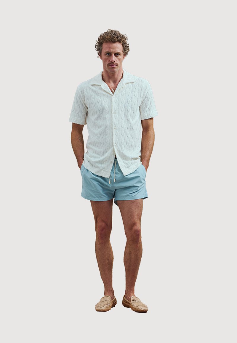 Witte gebreide shirt met korte mouwen, lichtblauwe shorts en beige instapschoenen; casual zomerkleding met een relaxte pasvorm.