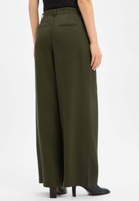 Olive green wide-leg trousers with a textured fabric, elastic waistband, and two back pockets, paired with black high-heeled shoes.