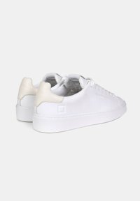 Sneakers bianchi in pelle con un tallone texturizzato color crema, suola piatta bianca e cuciture tono su tono. Lacci rotondi e design minimalista.
