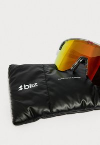 Spordiprillid, millel on oranžikad läätsed, asetatud mustale pehmele kotile, millel on sildid "bliz" ja "Performance Eyewear."