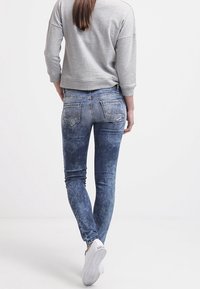 Jeans ajustados en un lavado azul desvanecido, con un corte entallado, sutiles desgastes y bolsillos traseros con detalles de costura. Combinados con un suéter gris.