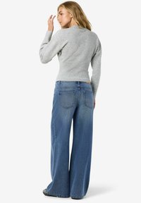 Suéter gris acanalado combinado con jeans de mezclilla azul de pierna ancha con una cintura alta, dos bolsillos traseros y un dobladillo sin terminar.