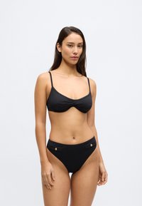 Σετ μαύρου μπικίνι που περιλαμβάνει μαλακό τριγωνικό τοπ με ρυθμιζόμενους ιμάντες και σλιπ με ψηλή μέση, διακοσμημένο με χρυσές λεπτομέρειες και υφασμάτινη υφή.